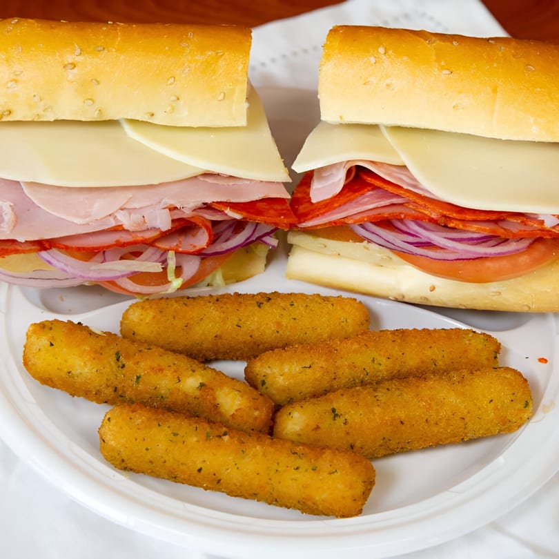 Two deli sandwiches with various meats, cheese, and vegetables, served with mozzarella sticks.