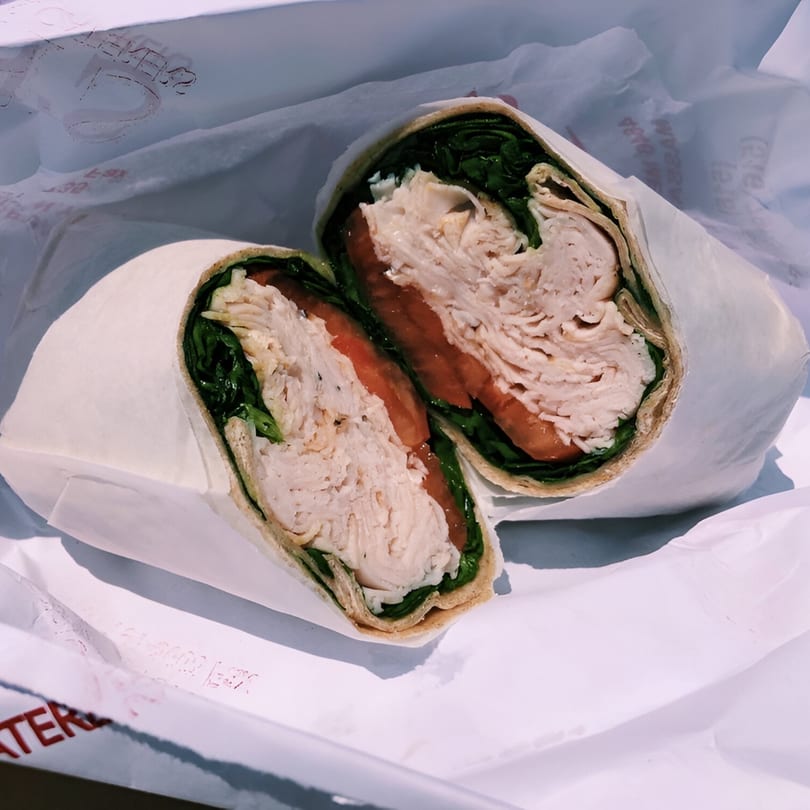 A Finn's Deli turkey wrap, cut in half, revealing sliced turkey, tomatoes, and lettuce.