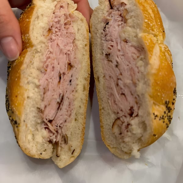 A Finn's Deli sandwich, cut in half, revealing generous layers of deli meat on a seeded bun.