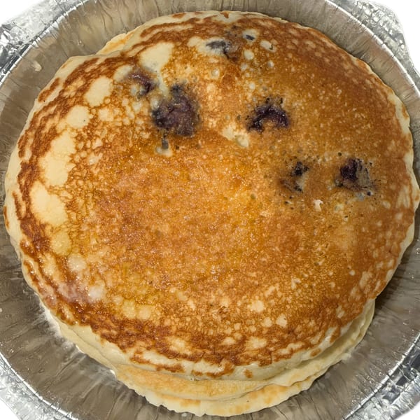 Stack of golden-brown blueberry pancakes in a silver foil takeout container from Finn's Deli.