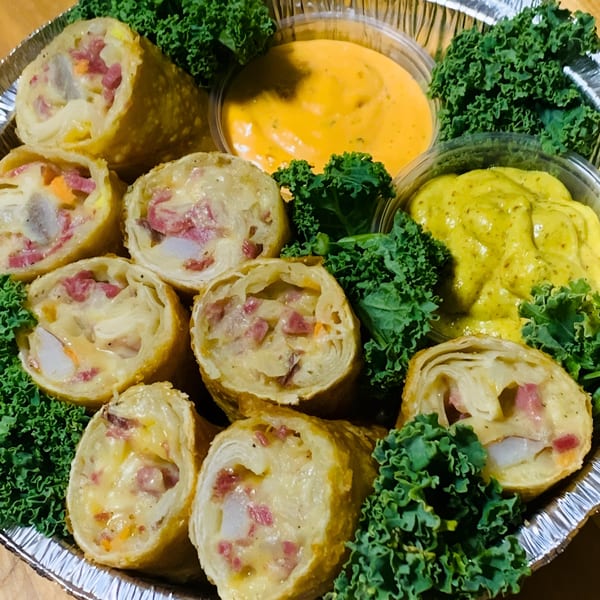 Finn's Deli egg rolls with meat, cheese, and vegetables, served with two dipping sauces and kale.